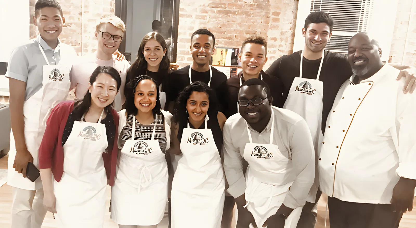 Group in aprons with their chef after a team cooking class