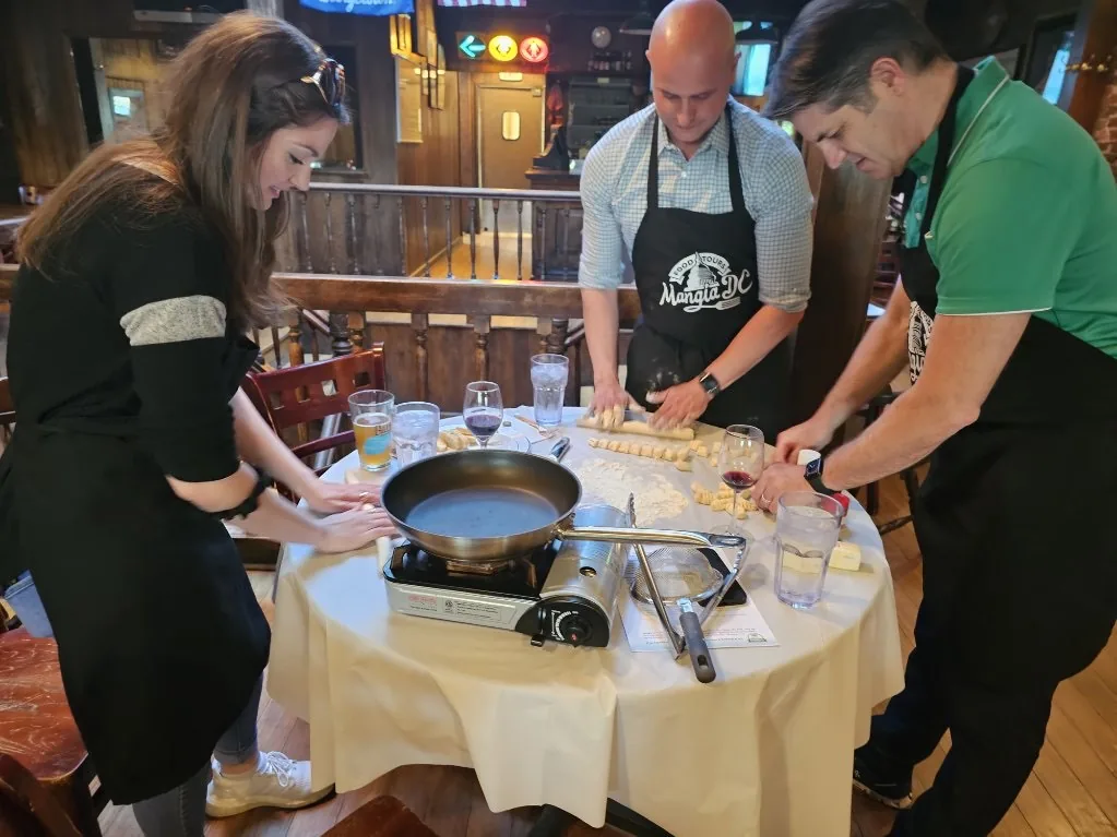 Three guests rolling fresh pasta around a table at a group cooking class