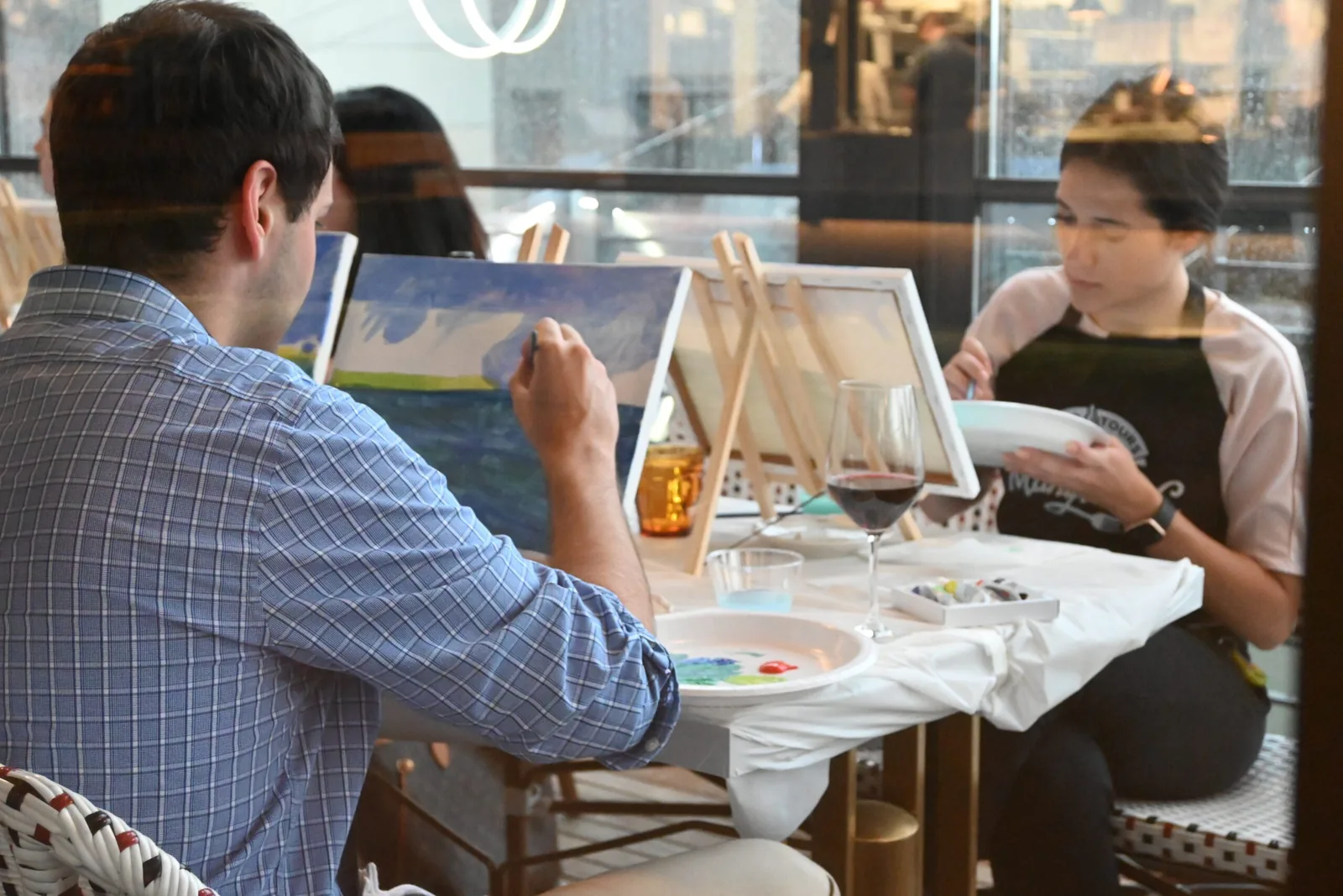 Guests painting a landscape at a paint and sip with a city view behind them